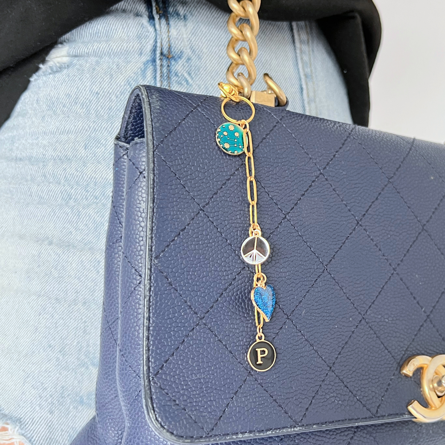 Blue quilted handbag with gold chain and charms, worn by a person in denim jeans.