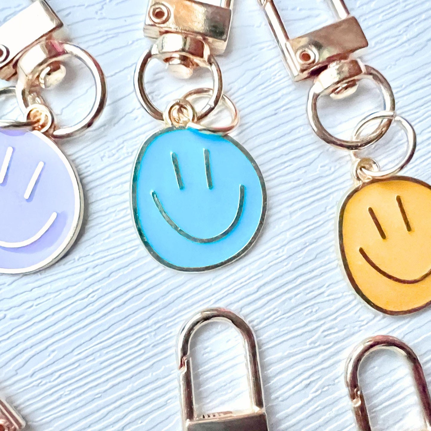 Three smiley face keychains in purple, blue, and yellow on a textured surface.