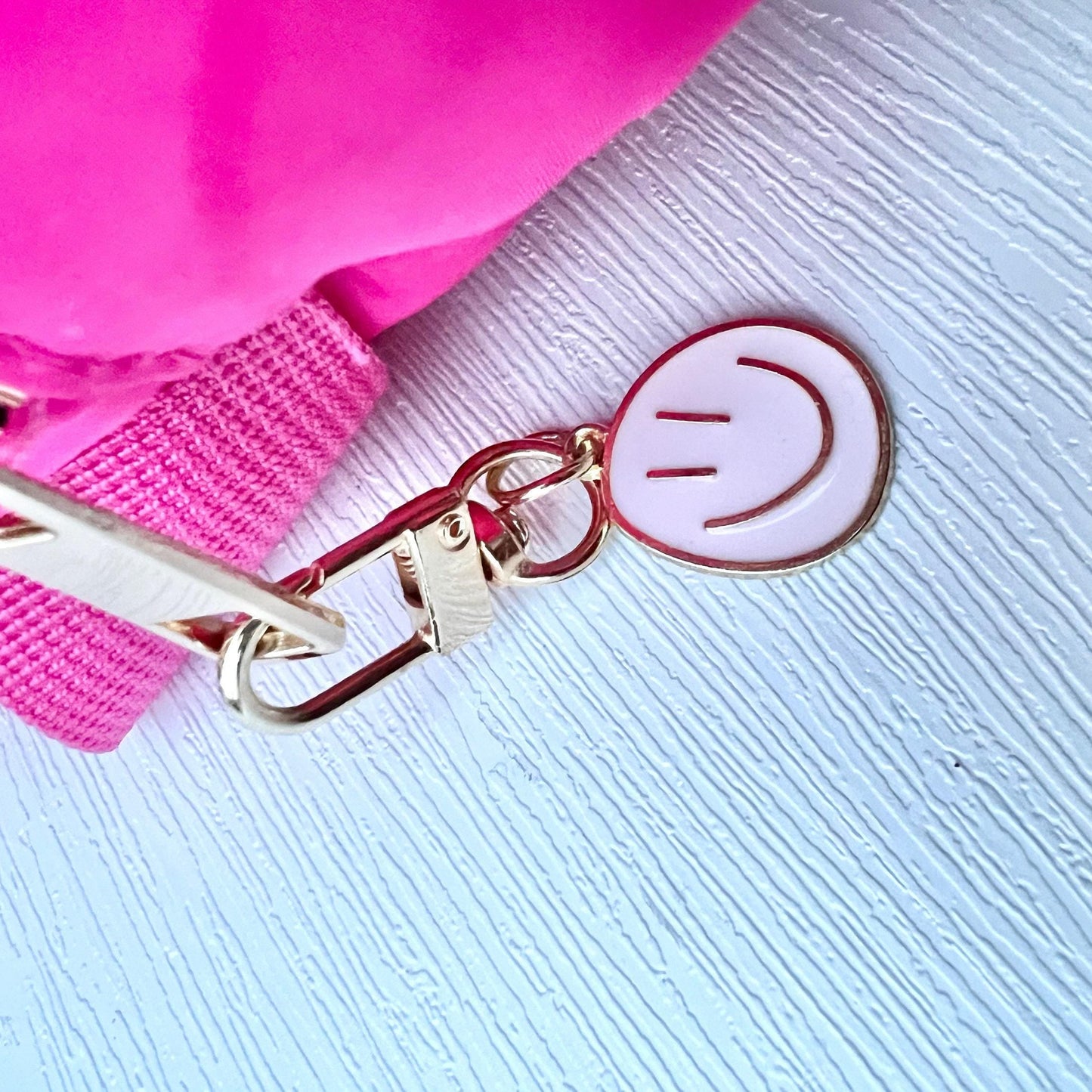 Pink bag with a smiley face keychain on a light blue textured background