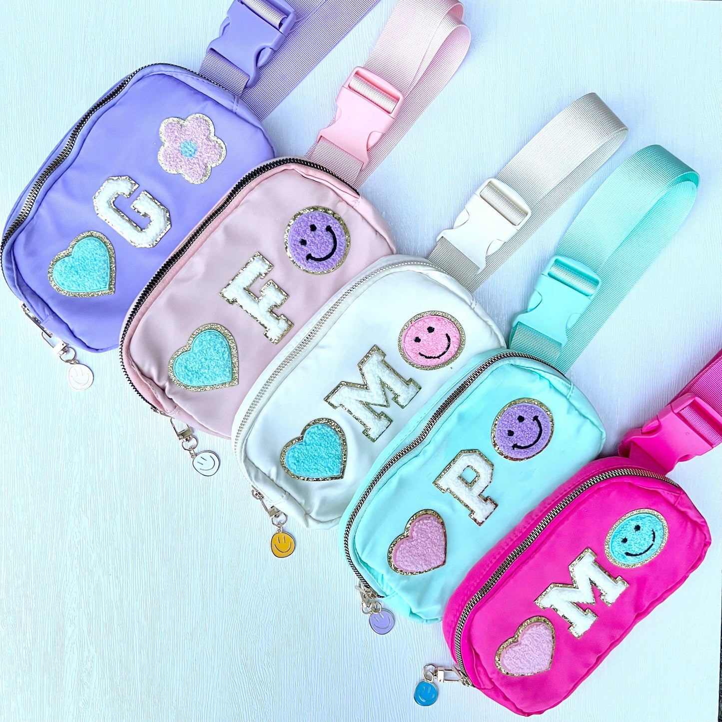 Four colorful fanny packs with decorative elements on a light blue background