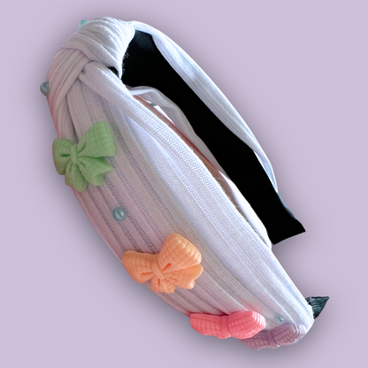 A white headband with colorful coquette bow charms and blue pearl rhinestones 