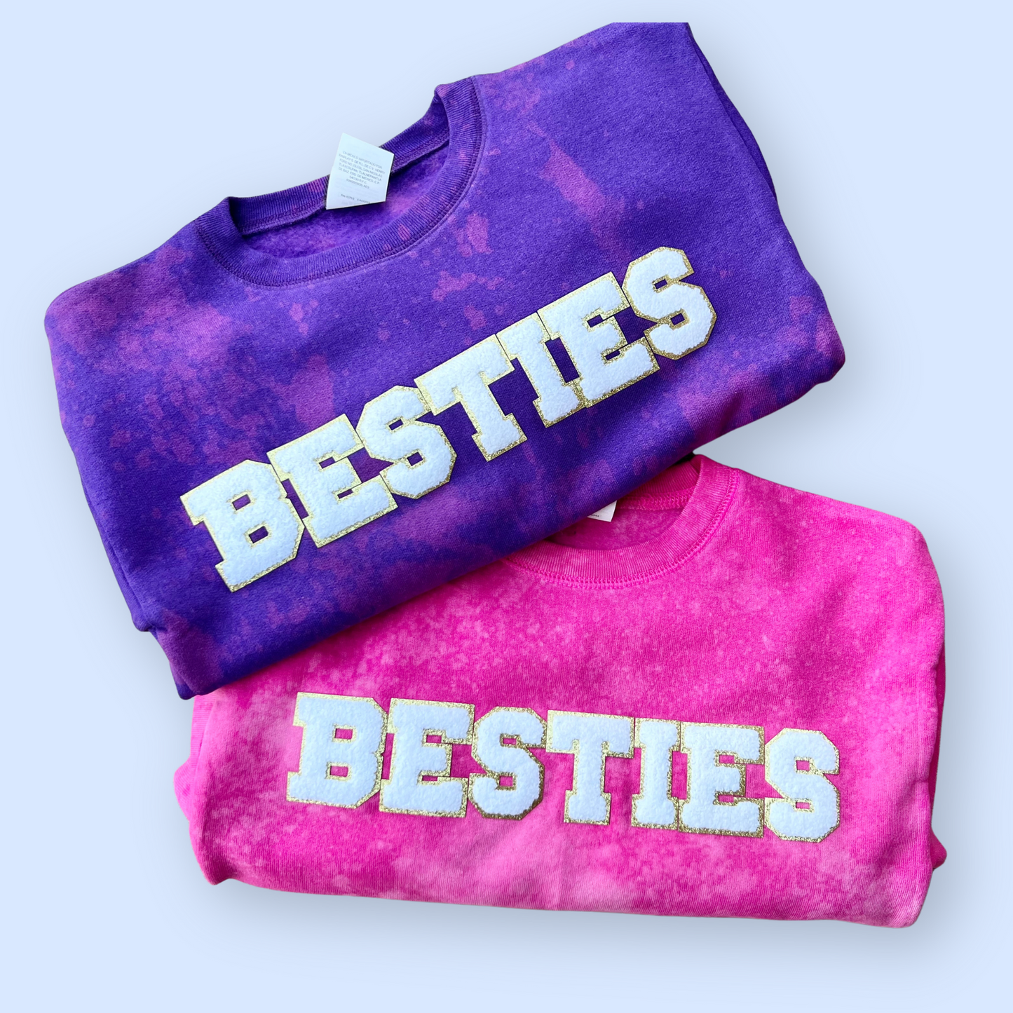 Two tie-dye sweatshirts, one purple and one pink, with 'BESTIES' on them in white  chenille patches