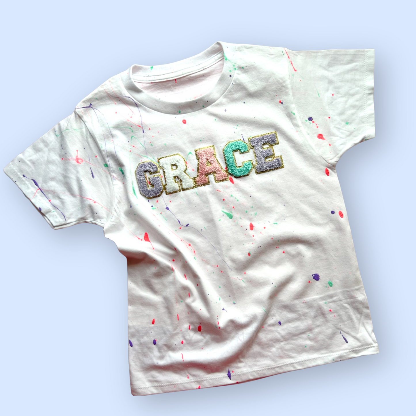 White t-shirt with 'GRACE' printed in colorful letters on a light blue background