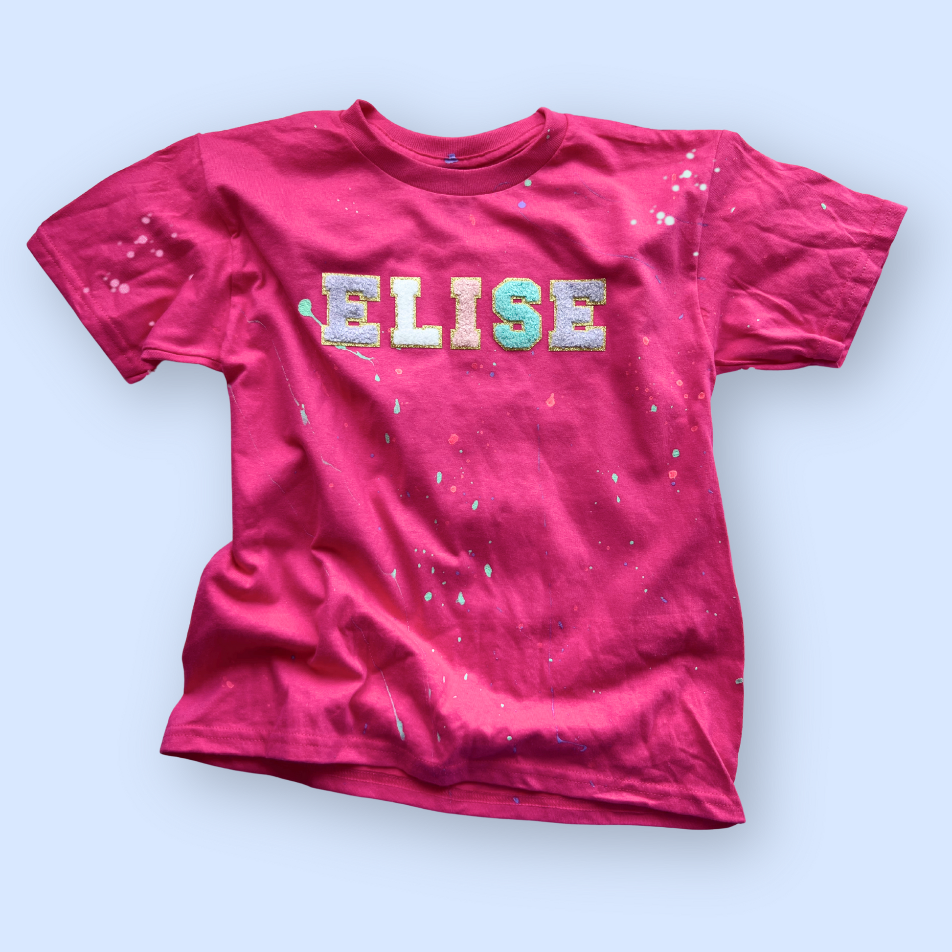 Pink t-shirt with 'ELISE' printed on it against a light blue background