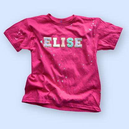 Pink t-shirt with 'ELISE' printed on it against a light blue background