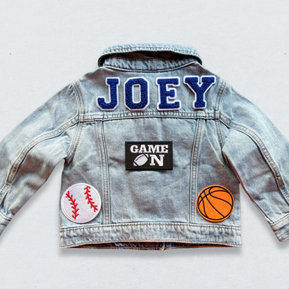 Denim jacket with 'JOEY' patch and sports-themed designs on a light gray background