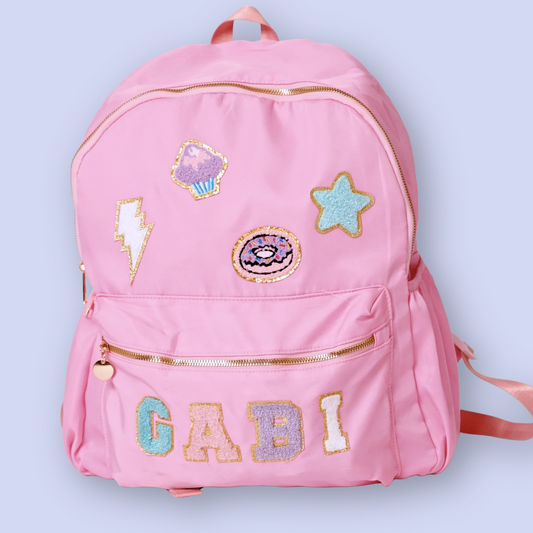 Pink backpack with decorative patches and the name 'Gabi' on a light blue background