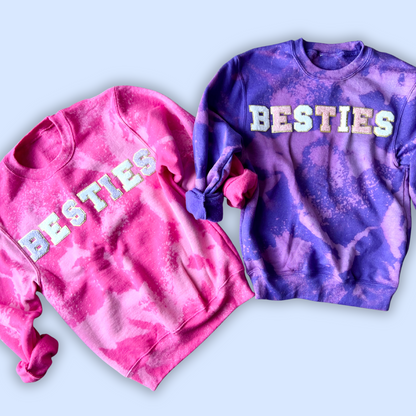 Two tie-dye sweatshirts, one pink and one purple, with 'BESTIES' text on a light blue background.