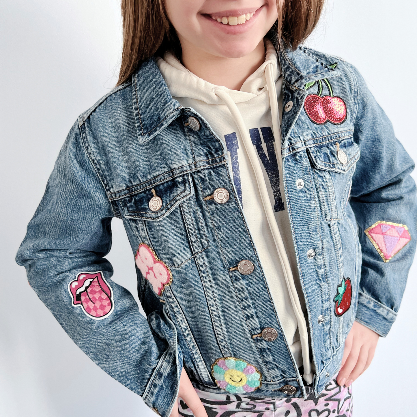 Child wearing a denim jacket with colorful patches on a white background
