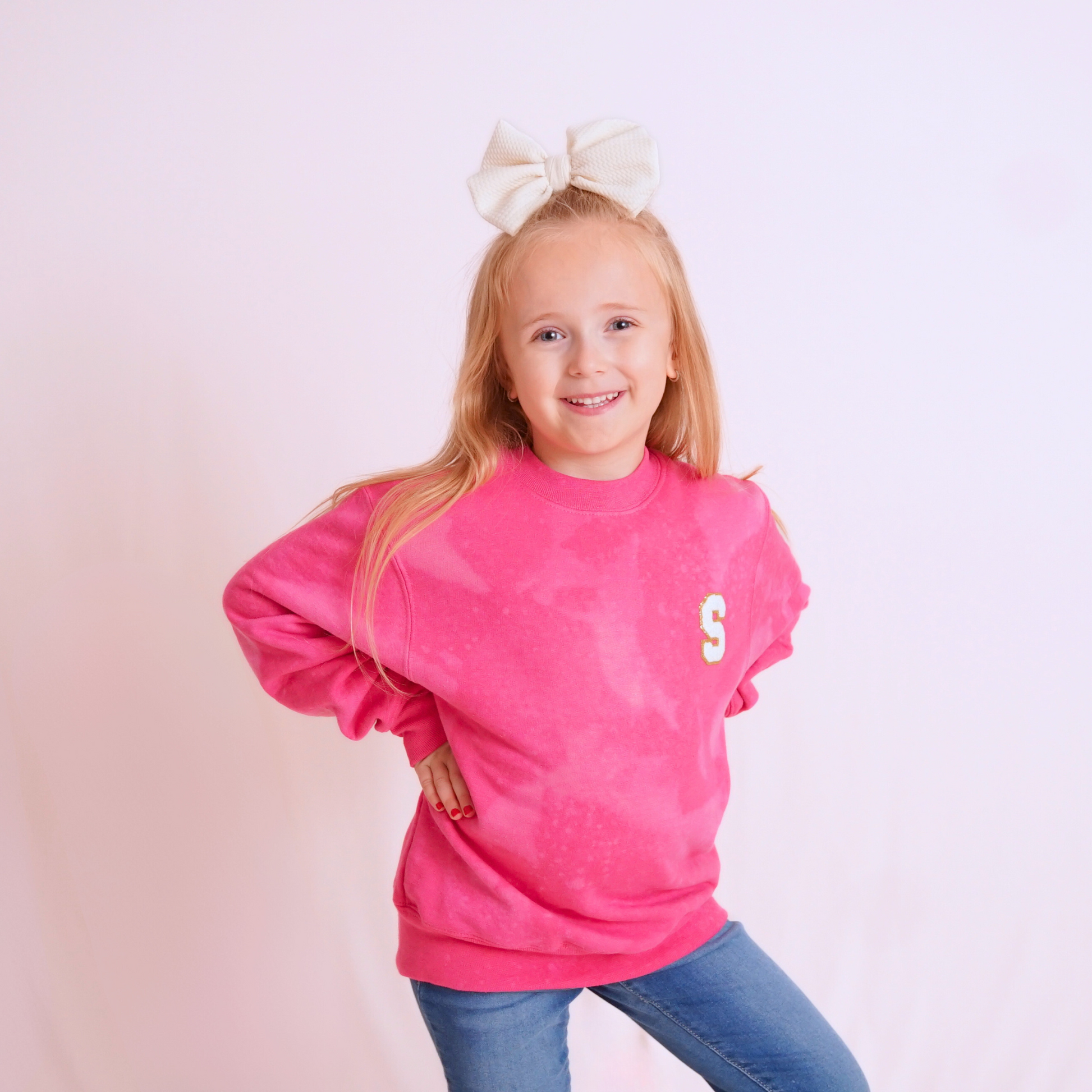 Young girl wearing a pink sweatshirt with a letter 'S' on a light pink background