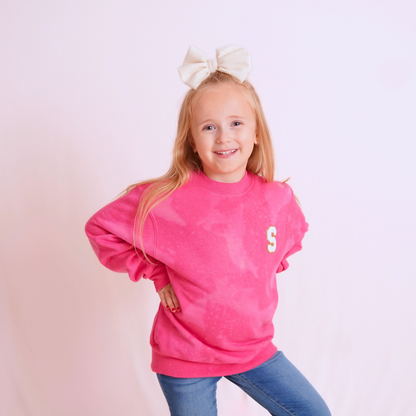 Young girl wearing a pink sweatshirt with a letter 'S' on a light pink background