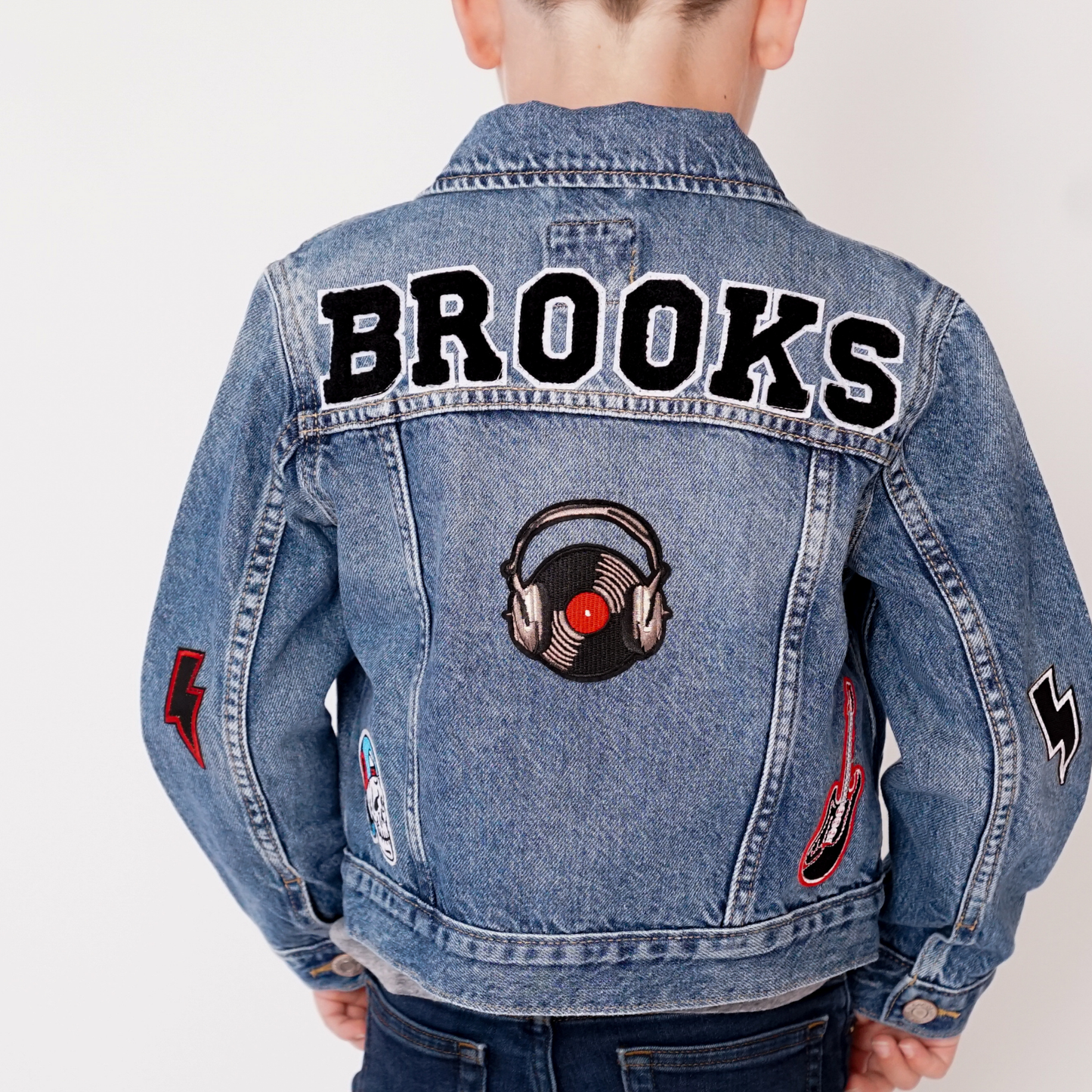 Denim jacket with 'Brooks' text and music-themed patches on a plain background