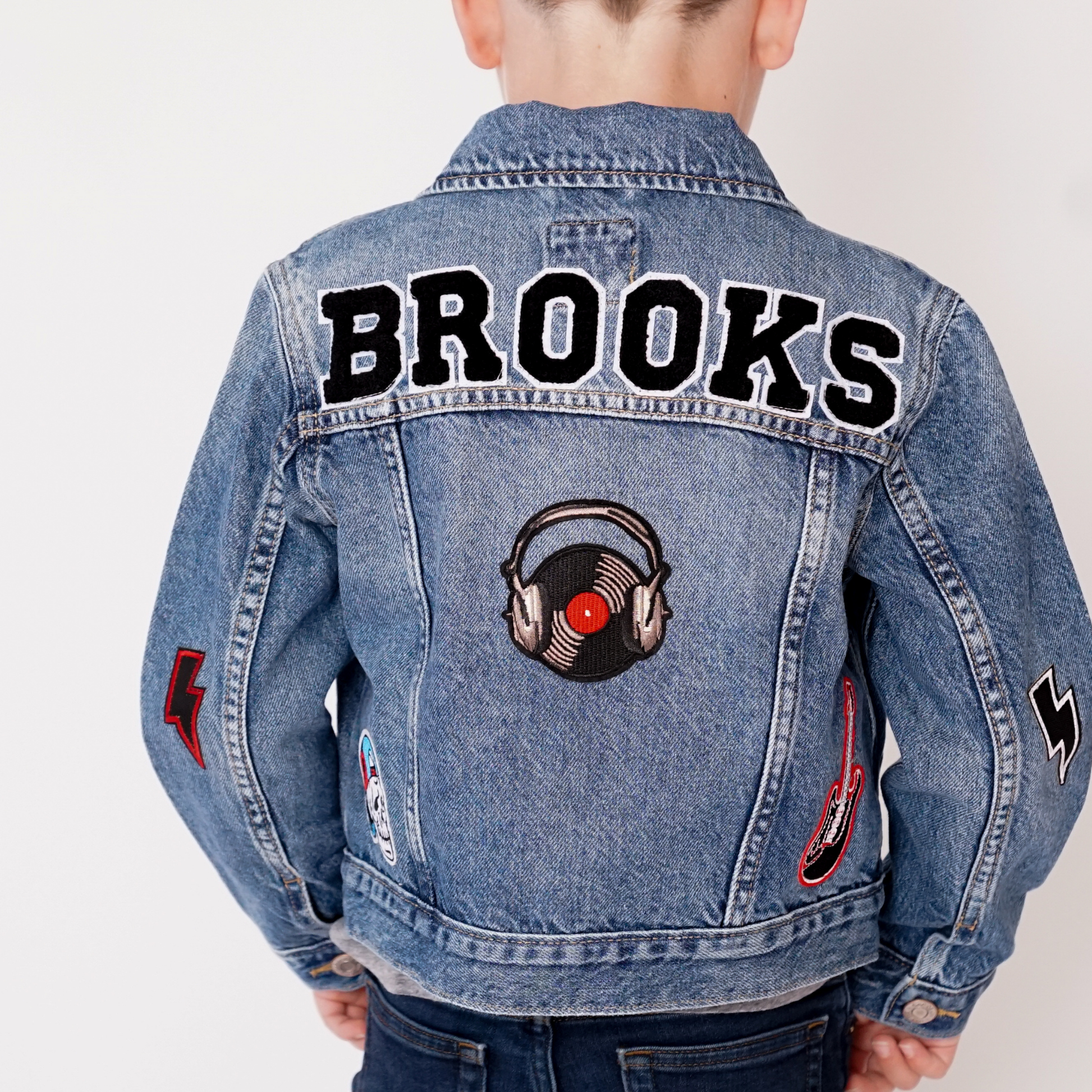 Denim jacket with 'Brooks' text and music-themed patches on a plain background