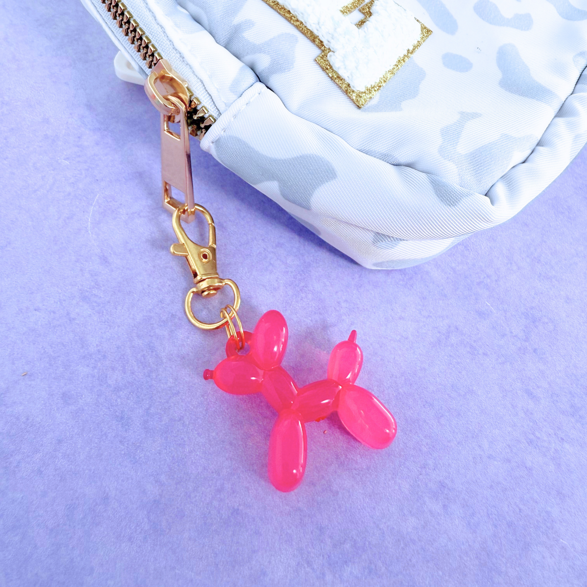 Pink balloon dog keychain attached to a white bag with gold chain on a purple background