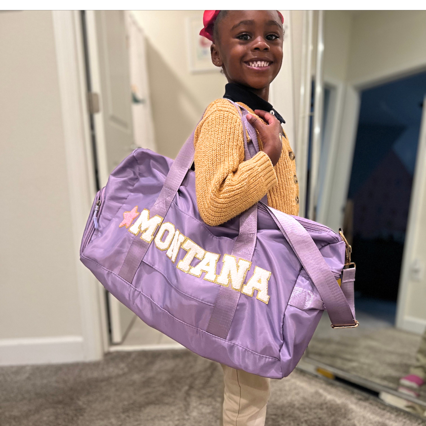 Girl holding purple duffle bag with name MONTANA and rainbow/sparkle patches.