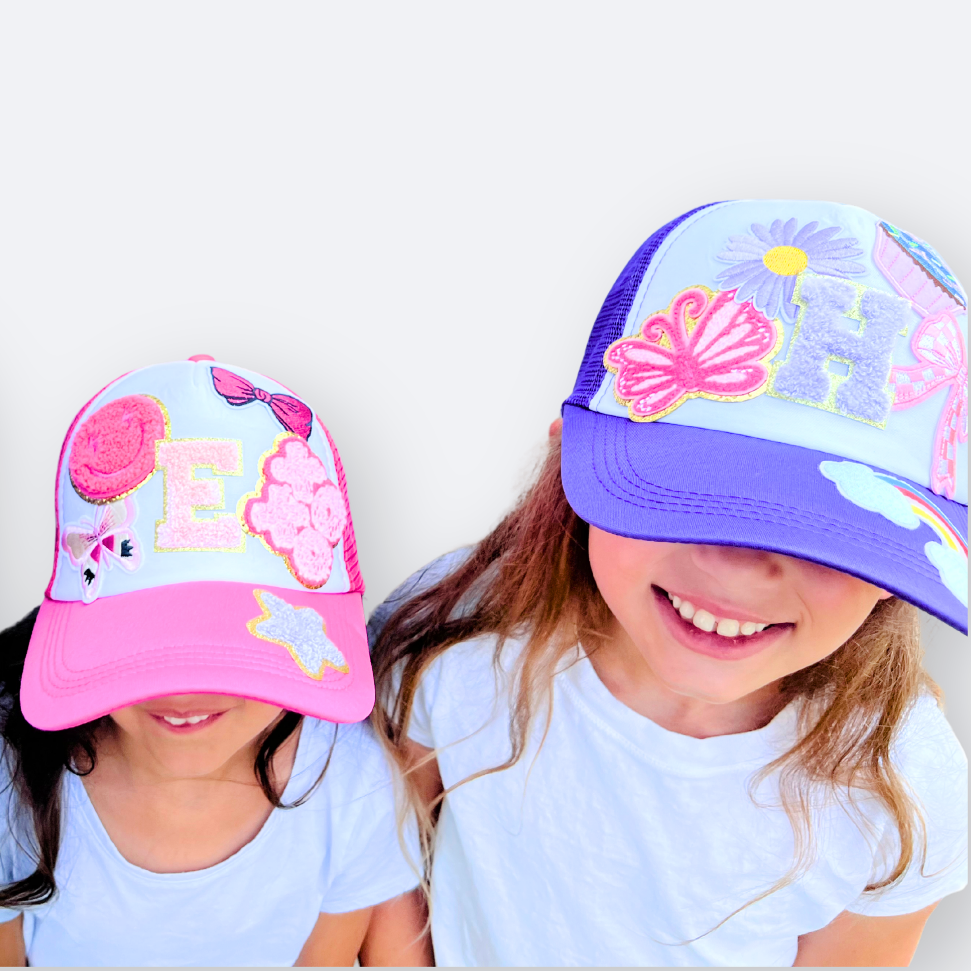 Two children wearing colorful baseball caps with floral and butterfly designs on a white background.