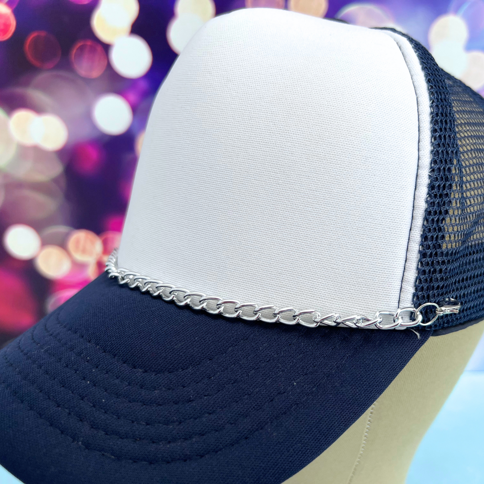 Navy and white cap with a chain detail against a colorful blurred background