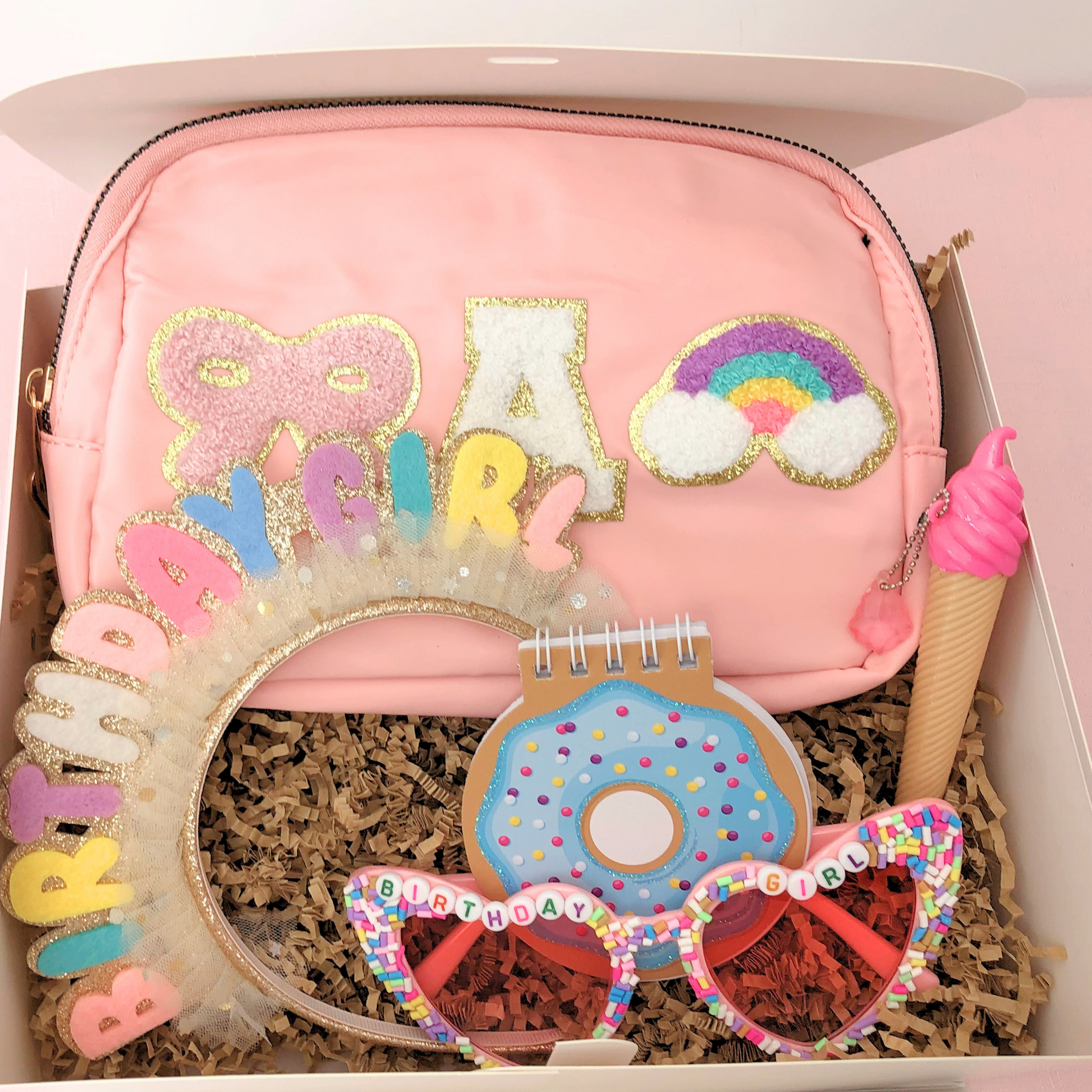 Pink and pastel set – Light pink bag with rainbow and heart patches, glasses, notepad, headband, and pen in matching tones.