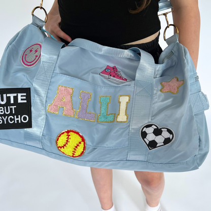 Blue duffle bag worn over shoulder with name ALLI and various sports patches.