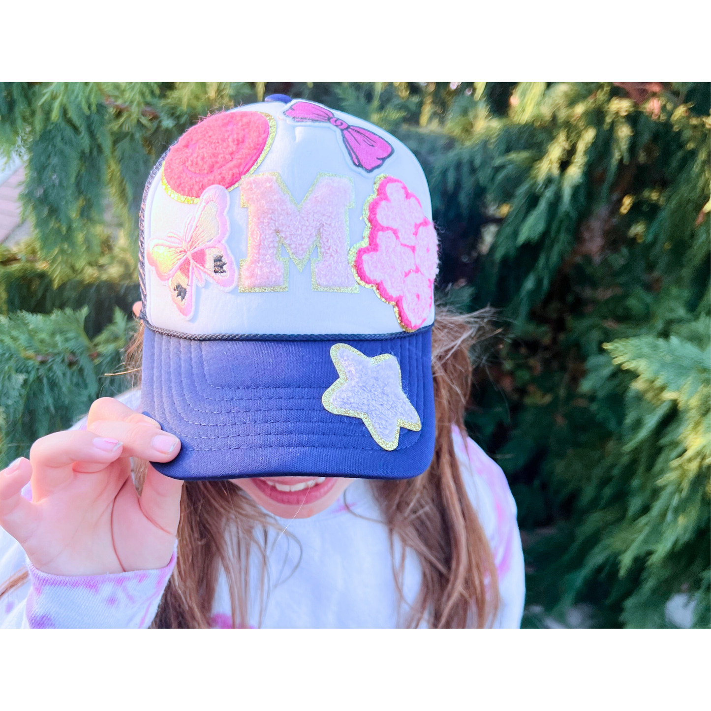 Colorful cap with pink floral design held by a person against a green foliage background