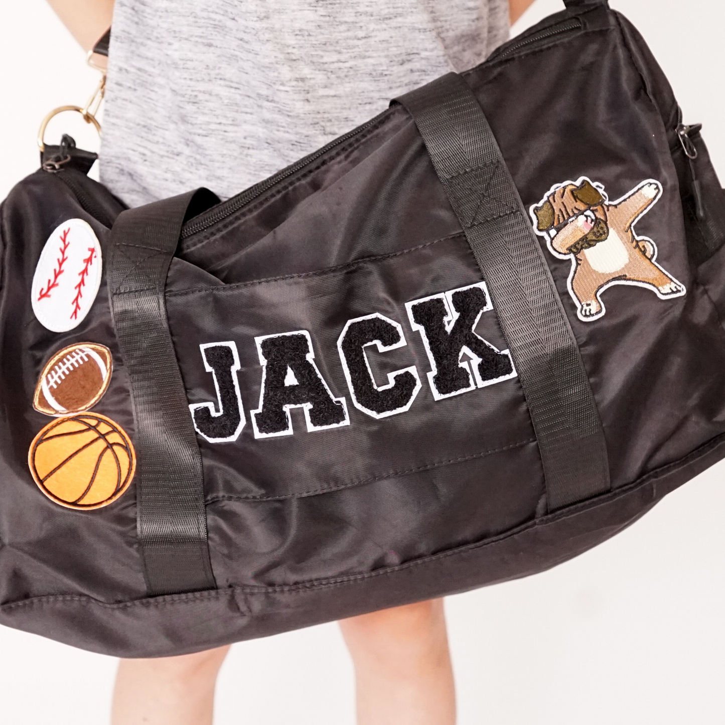 Black duffle bag held by child with name JACK and baseball, basketball, and star patches