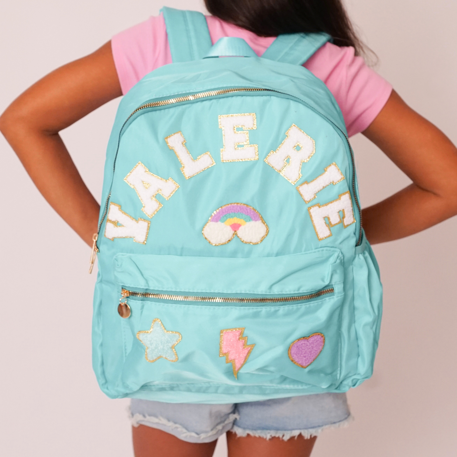 Person wearing a turquoise backpack with decorative patches and 'Valerie' text.