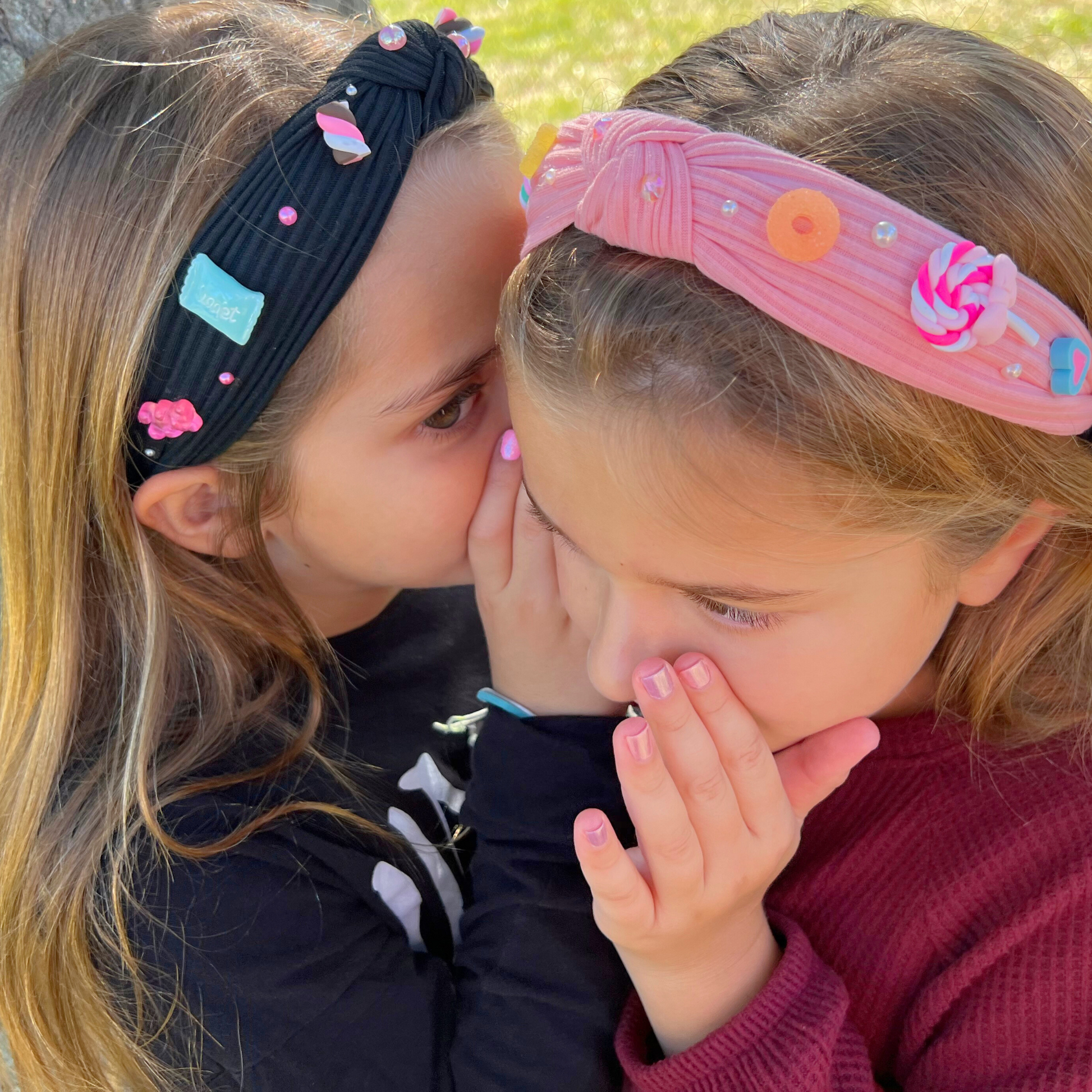 two girls whispering to each other wearing trendy charm headbands with candy charms 