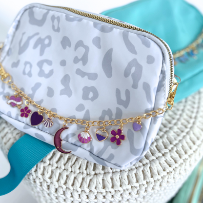 White cosmetic bag with gold chain and charms on a textured surface
