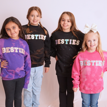 Four children wearing 'BESTIES' sweatshirts on a plain background