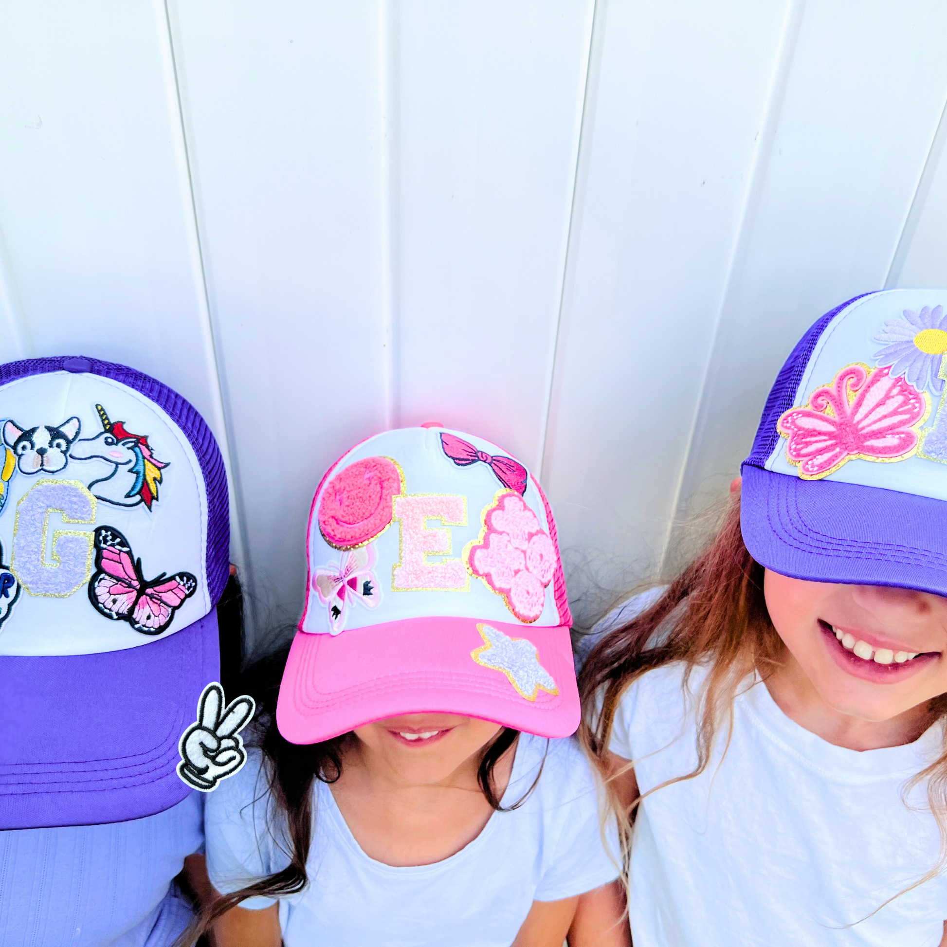 Three children wearing colorful baseball caps with various designs against a white background