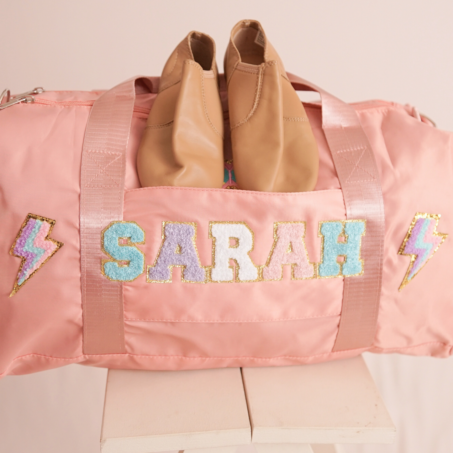 Pink duffle bag on bed with name SARAH and lightning bolt patches.
