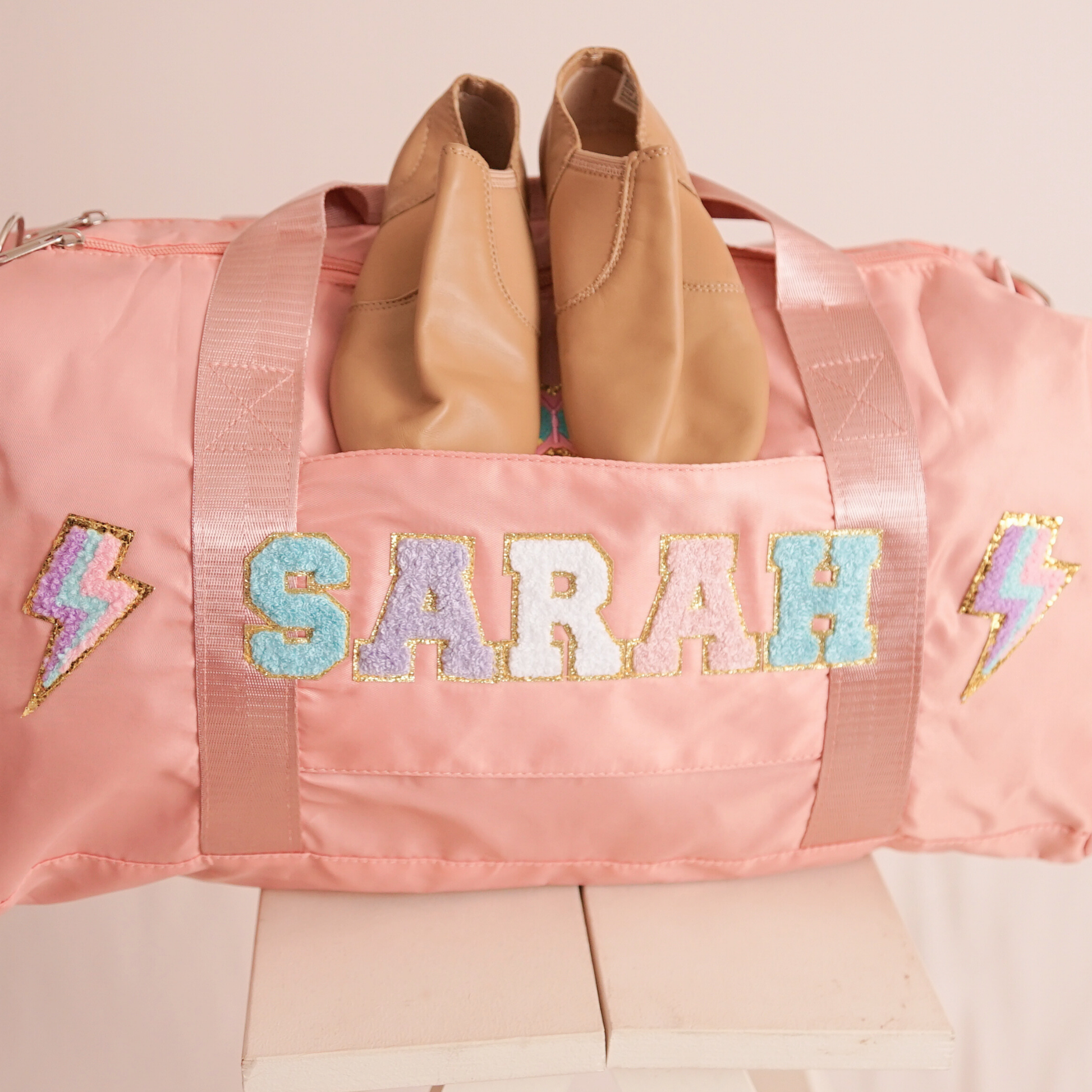 Pink duffle bag on bed with name SARAH and lightning bolt patches.