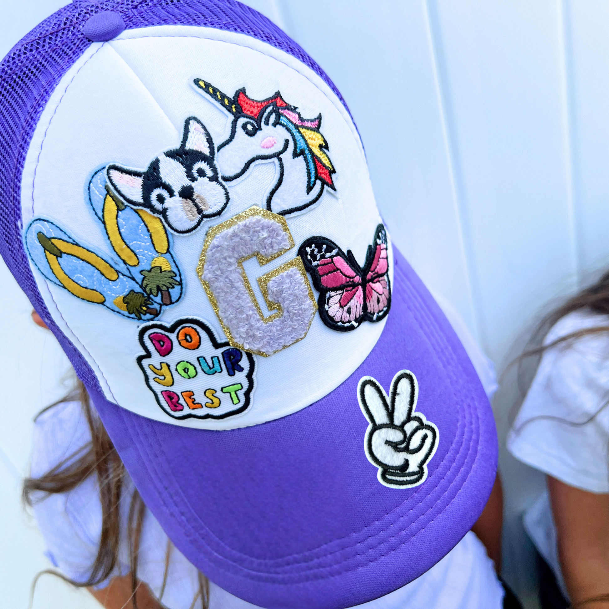 Purple and white cap with various patches including a unicorn, dog, butterfly, and motivational text.