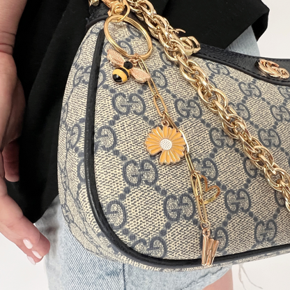 Designer handbag with gold chain and charms, featuring a recognizable brand logo.