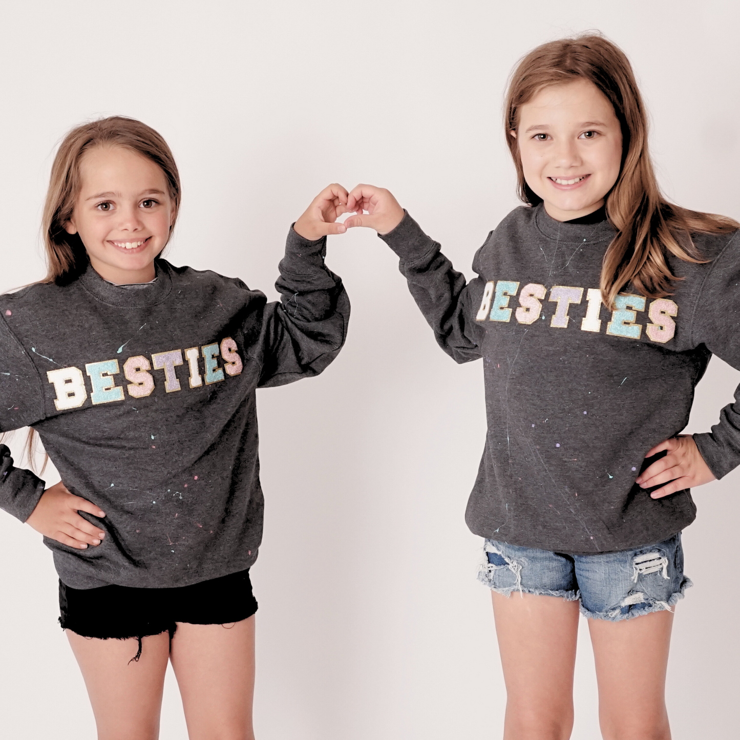 Two girls wearing matching gray sweatshirts with 'BESTIES' text on a white background
