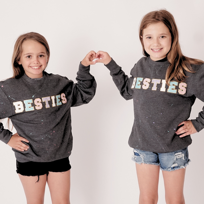 Two girls wearing matching gray sweatshirts with 'BESTIES' text on a white background