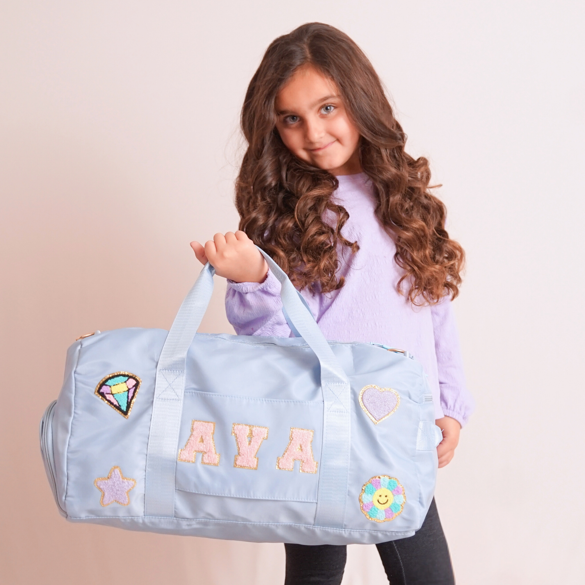 Young girl holding baby blue duffle bag with name “AVA” and heart patches