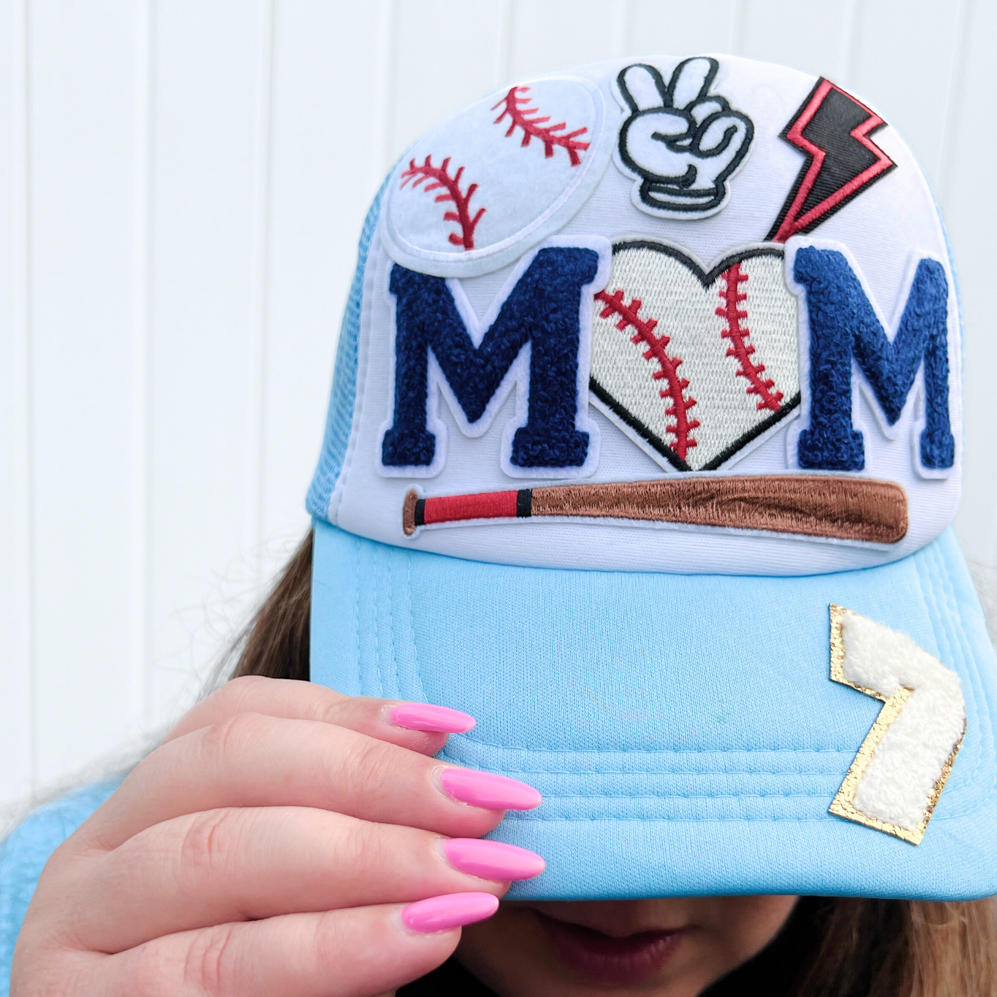 Baseball-themed cap with decorative elements held by a person with pink nails.