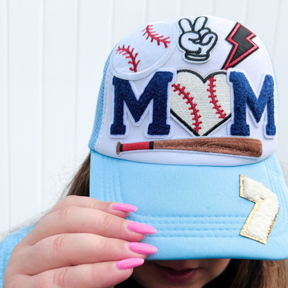 Baseball-themed cap with decorative elements held by a person with pink nails.