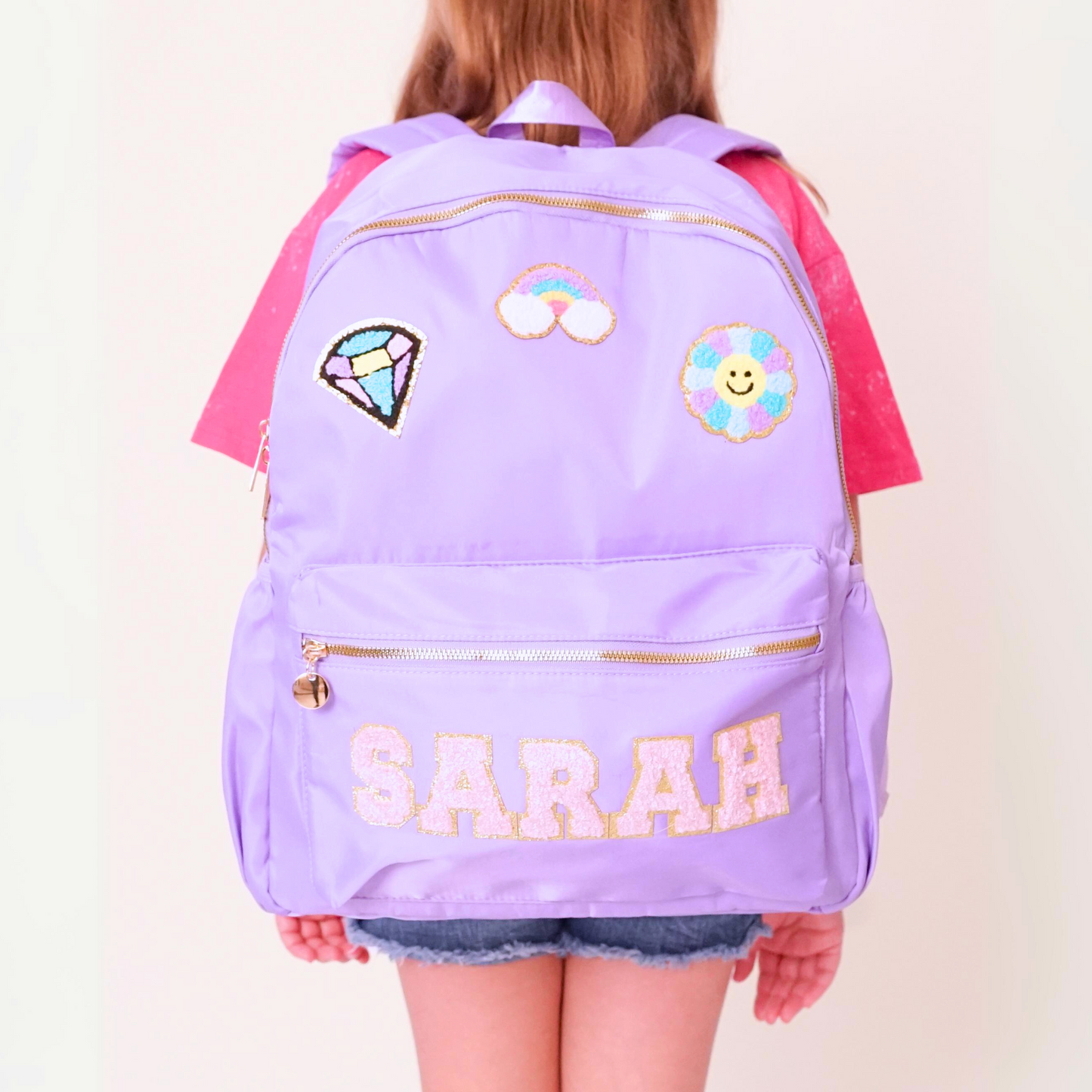 Purple backpack with decorative patches and the name 'SARAH' on a plain background