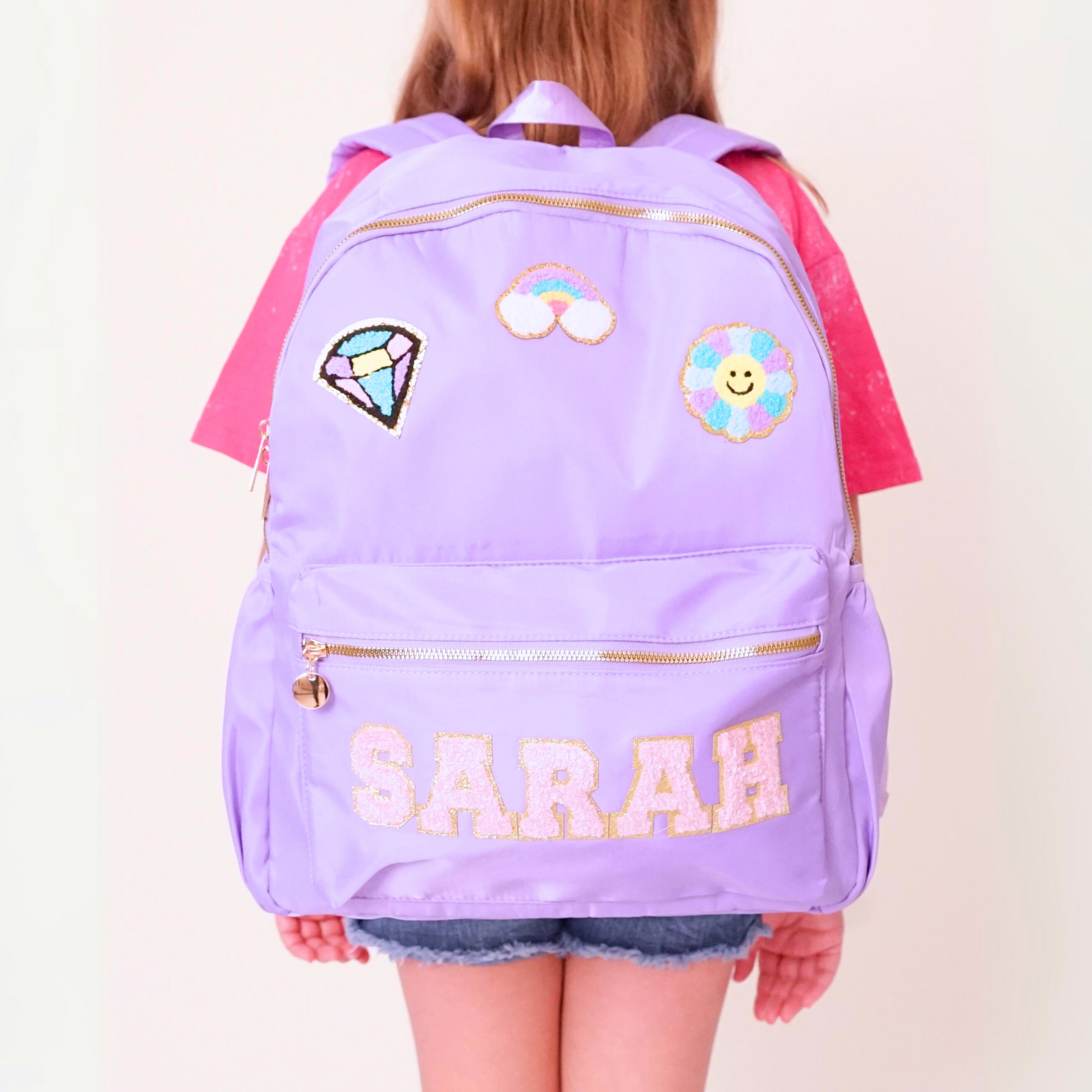 Purple backpack with decorative patches and the name 'SARAH' on a plain background
