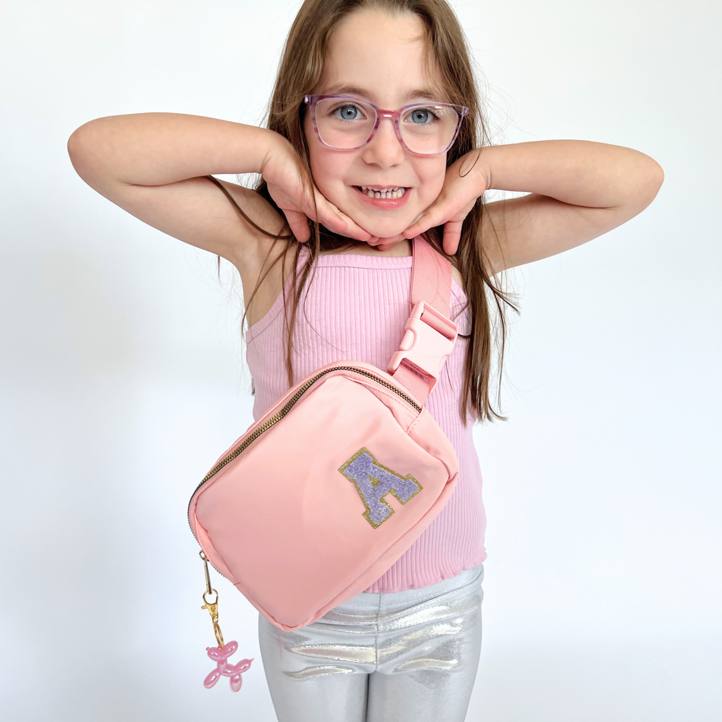 Girl wearing pink fanny pack with A patch smiling with arms up