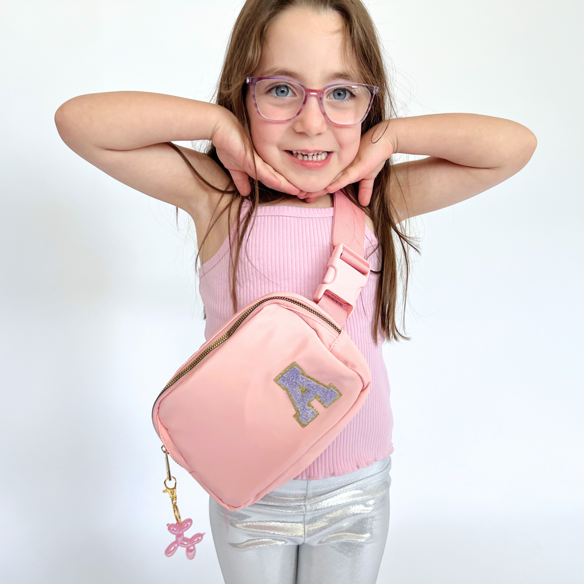 Girl wearing pink fanny pack with A patch smiling with arms up
