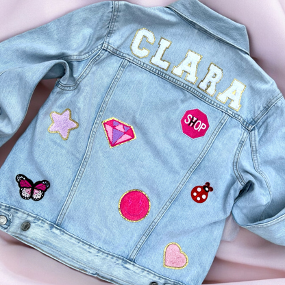 Denim jacket with colorful patches including stars, a butterfly, and text on a pink background