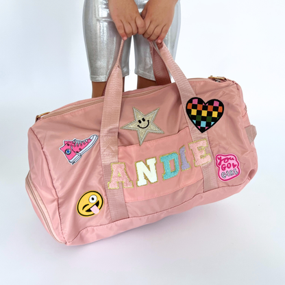 Pink duffle bag with colorful patches and name ANDIE on the front.