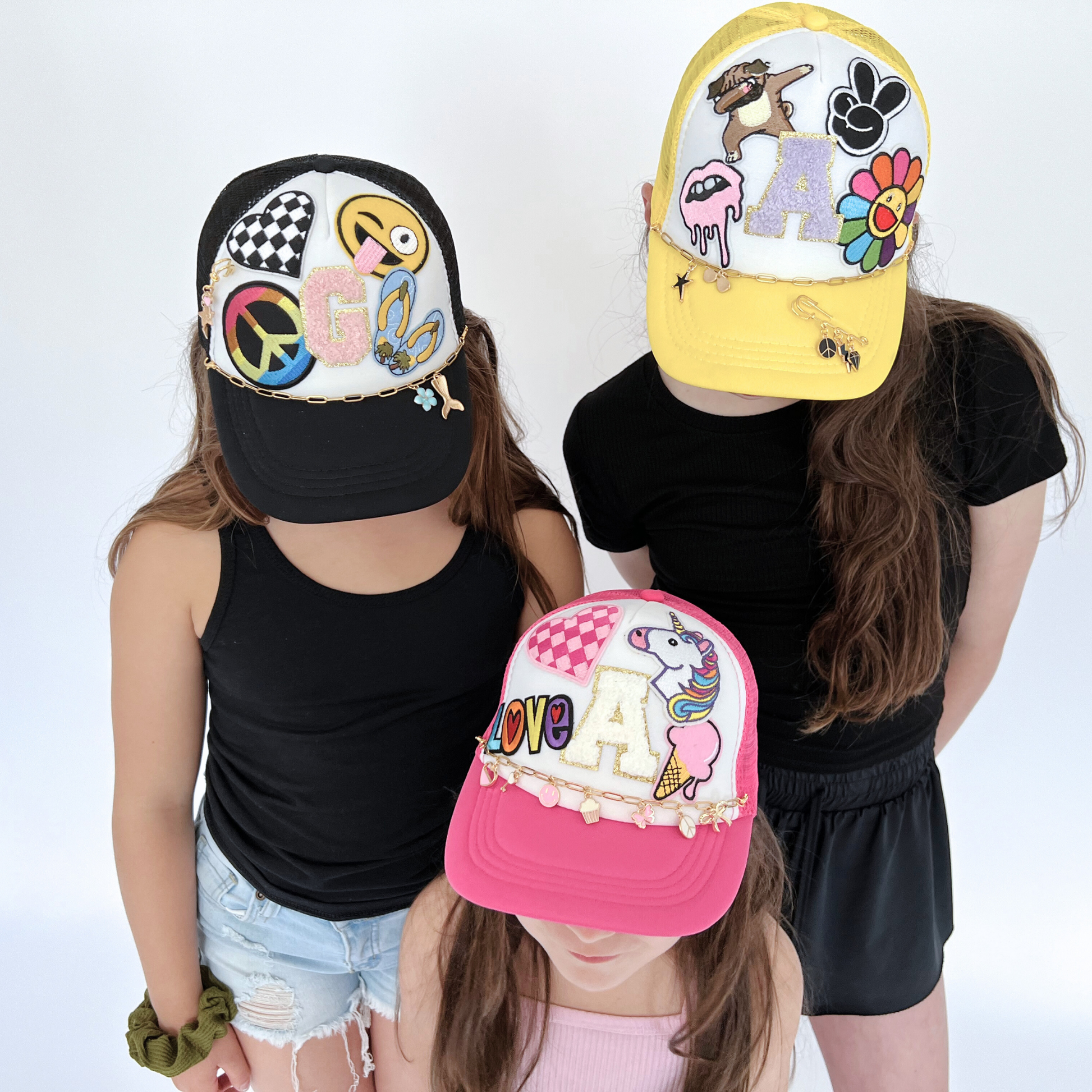 Three children wearing colorful baseball caps with various designs on a white background