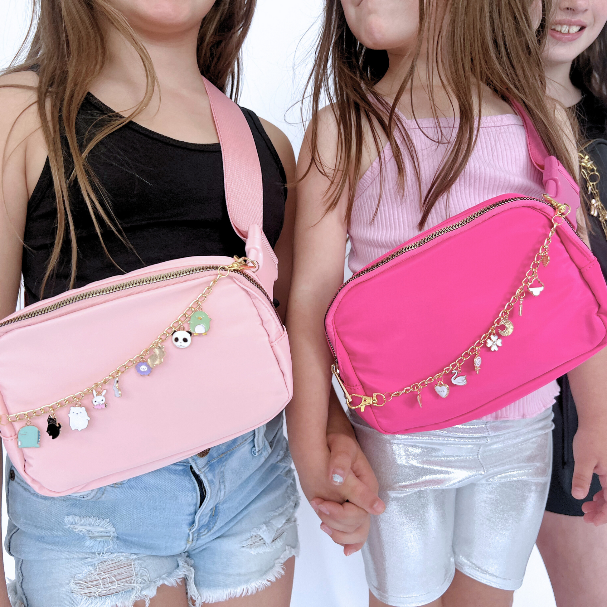 Two children holding pink waist bags with charm straps on a white background