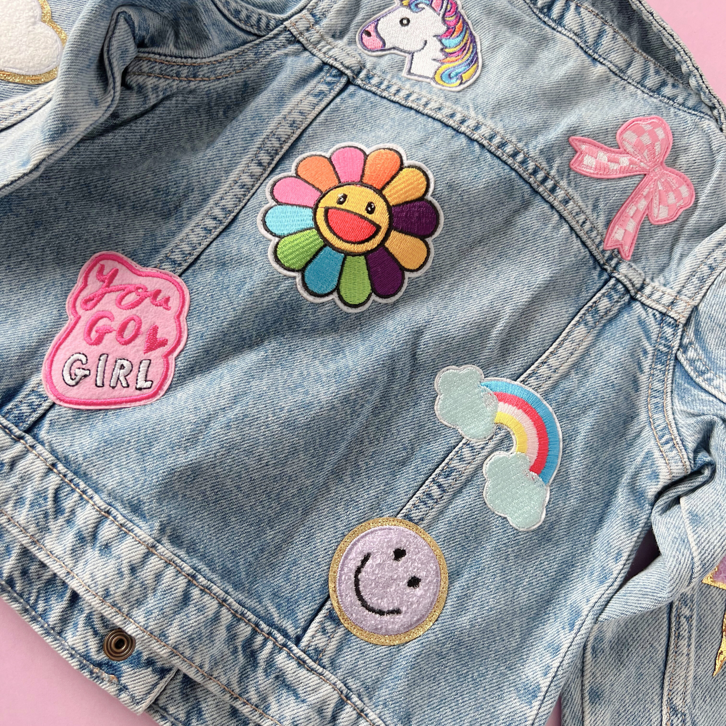 Denim jacket with colorful patches including a rainbow flower, cloud, smiley face, and 'You Got Girl' text.