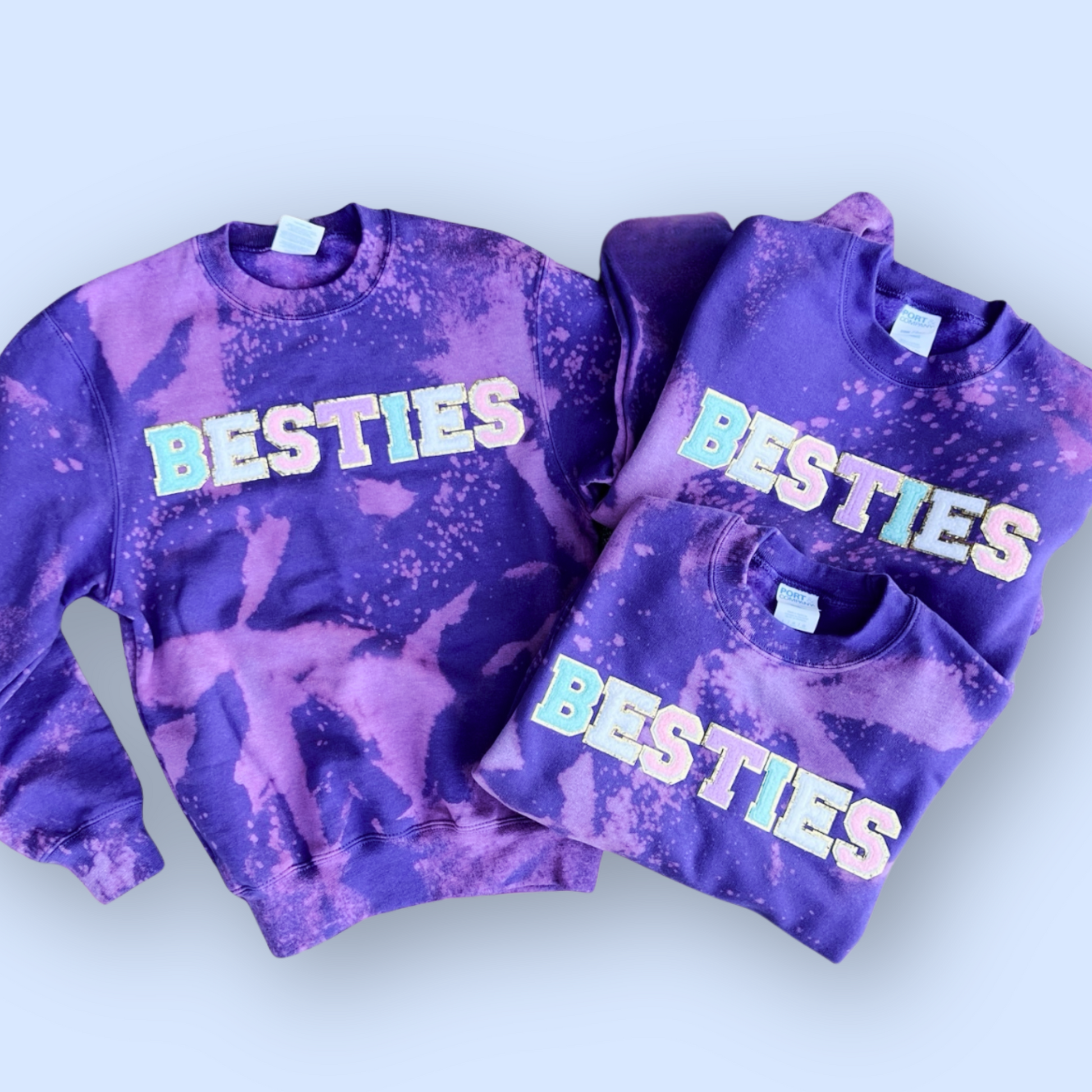 Two purple tie-dye sweatshirts with 'BESTIES' text on a light blue background