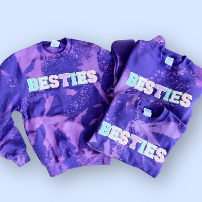 Two purple tie-dye sweatshirts with 'BESTIES' text on a light blue background